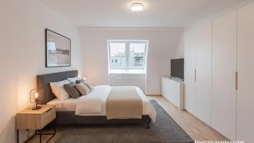 Helles Schlafzimmer mit Holzboden, großem Kleiderschrank und gemütlichem Bett unter einem Dachfenster.