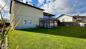 Großzügiger Gartenbereich mit Rasenfläche und einem Wintergartenanbau am Haus.