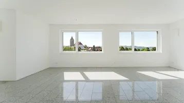 Geräumiger, heller Wohnraum mit glänzenden Fliesen und Panoramafenstern mit Blick auf die Kirche und Landschaft.