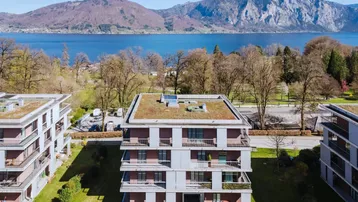 Moderne Wohngebäude mit Gründächern und Balkonen, umgeben von Natur mit See- und Bergblick.