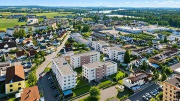 Luftaufnahme einer Wohnsiedlung mit modernen Gebäuden, umgeben von grünen Feldern und einem See.