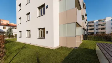 Moderne Wohnanlage mit weißer Fassade, gepflegtem Rasen und sonnigem Außenbereich.