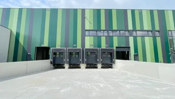Moderne Industriefassade mit mehreren Laderampen und einer klaren, gestreiften Farbgebung in Grüntönen.