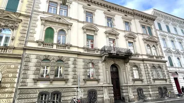 Historisches Gebäude mit reich verzierter Fassade, klassischen Fenstern und einem schmiedeeisernen Balkon.
