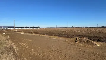 Weites, unbebautes Grundstück unter blauem Himmel, bereit für die Bebauung, mit Gebäuden in der Ferne.