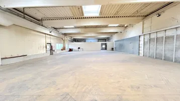 Geräumige, leere Lagerhalle mit hohen Decken, Betonboden und Oberlichtern für natürliches Licht.