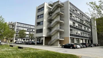 Modernes Bürogebäude mit markanter Außentreppe und Parkplätzen im Freien unter blauem Himmel.