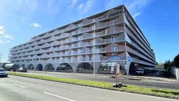 Modernes Mehrfamilienhaus mit geschwungenen Balkonen und großen Glasfronten an einer belebten Straße.