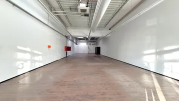 Geräumiger, leerer Gewerberaum mit hohen Decken, Holzboden und Oberlichtern für viel Tageslicht.