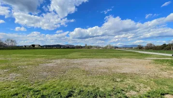 Weitläufiges grünes Feld unter blauem Himmel mit weißen Wolken und Bergblick in der Ferne.