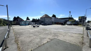 Weitläufiger Außenbereich mit asphaltierter Fläche und umliegenden Gebäuden unter blauem Himmel.