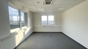 Heller Büroraum mit Teppichboden, abgehängter Decke und Klimaanlage, bietet viel Tageslicht.