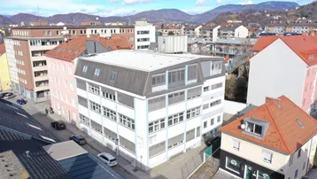 Luftaufnahme eines modernen Bürogebäudes in städtischer Umgebung mit Bergen im Hintergrund.