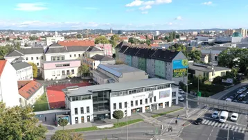 Luftaufnahme eines modernen Geschäftsgebäudes mit umliegender Stadtlandschaft und Verkehrskreuzung unter blauem Himmel.