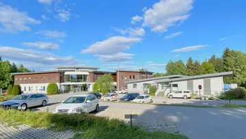 Außenansicht eines modernen Bürokomplexes mit großem Parkplatz unter blauem Himmel.