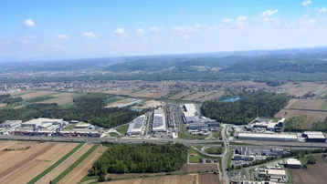 Luftaufnahme eines Industriegebiets umgeben von Feldern und Wäldern unter blauem Himmel.
