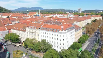 Luftaufnahme einer Stadt mit roten Dächern, grünen Bäumen und Bergen im Hintergrund, die eine weite Aussicht bietet.