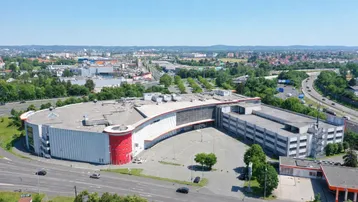 Luftaufnahme eines großen modernen Geschäftsgebäudes mit weitläufigem Parkplatz und umliegender Stadtlandschaft.