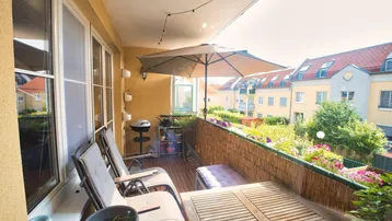 Möblierter Balkon mit Holzboden, Sonnenschirm und Blick auf die umliegenden Gebäude und Gärten.