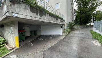 Einfahrt zur Tiefgarage mit Rolltor und angrenzendem Gebäude in schattiger Umgebung.