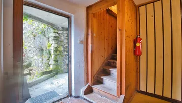 Eingangsbereich mit Holztreppe und Zugang zu einem begrünten Außenbereich mit Steinmauern.