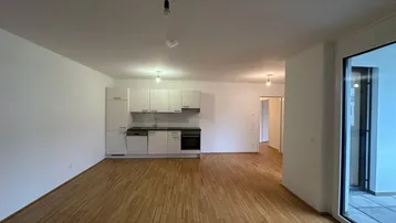 Heller offener Wohnbereich mit integrierter Küchenzeile, Parkettboden und Zugang zum Balkon.