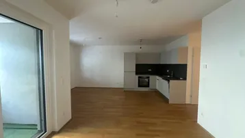 Heller Wohn-Essbereich mit Parkettboden, offener Küche und Zugang zu einem Balkon.