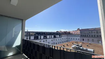 Sonniger Balkon mit Blick auf umliegende Gebäude und Dächer der Stadt.
