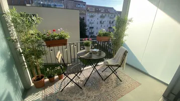 Sonniger Balkon mit gemütlichen Gartenmöbeln, Pflanzen und Blick auf die Stadt.