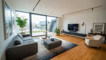 Modernes Wohnzimmer mit großen Fenstern, Holzboden und Blick auf das Wasser.