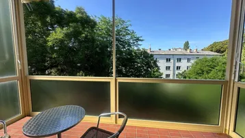 Verglaster Balkon mit Sitzgelegenheiten und Blick ins Grüne sowie auf umliegende Gebäude.