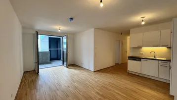 Heller Wohn- und Essbereich mit Parkettboden, integrierter Küchenzeile und Zugang zu einem Balkon.