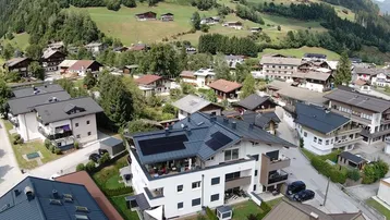 Luftaufnahme eines modernen Wohngebäudes mit Solaranlage in alpiner Umgebung.