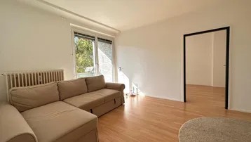 Helles Wohnzimmer mit beigem Sofa, Holzfußboden und Zugang zu einem Außenbereich.