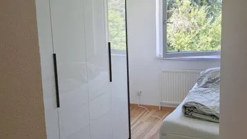 Schlafzimmer mit modernem weißen Kleiderschrank, Bett und Blick ins Grüne.