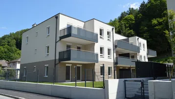 Modernes Mehrfamilienhaus mit Balkonen und Terrassen in grüner Hanglage.