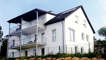 Modernes Wohnhaus mit weißer Fassade, Satteldach und mehreren Balkonen in Hanglage.