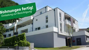 Modernes Mehrfamilienhaus mit weißer Fassade, Balkonen und grüner Umgebung.