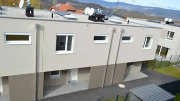 Rückansicht eines modernen Gebäudes mit Flachdach, Satellitenschüsseln und bergiger Landschaft im Hintergrund.