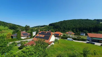Weitläufiger Blick über eine grüne Hügellandschaft mit Wohnhäusern und Solaranlagen auf den Dächern.