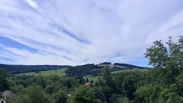 Weitläufiger Blick über grüne Hügel und Wälder unter einem blauen Himmel mit Wolken.