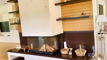 Moderner Kamin als Raumteiler mit Holzverkleidung und dunklem Holzboden im Wohnbereich.