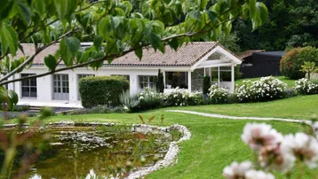 Idyllischer Gartenbereich mit Teich und Blick auf das charmante Landhaus, umgeben von blühenden Pflanzen.