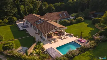 Luftaufnahme eines luxuriösen Anwesens mit großem Pool, überdachter Terrasse und weitläufigem Gartenbereich.