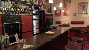 Gemütliche Bar mit dunklem Holztresen, Flaschenregalen und Hängelampen, bereit für Gäste.