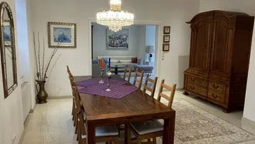 Geräumiges Esszimmer mit großem Holztisch, Kronleuchter und Blick in den Wohnbereich.