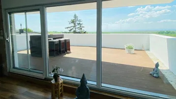 Große Schiebetüren öffnen sich zu einer weitläufigen Holzterrasse mit weitem Blick in die Landschaft.