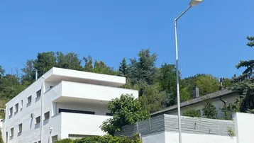 Moderne weiße Architektur mit mehreren Etagen und Garagen, umgeben von üppigem Grün unter blauem Himmel.