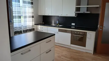 Moderne Küche mit weißen Schränken, dunkler Arbeitsplatte und hellem Laminatboden.