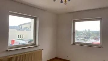 Helles Schlafzimmer mit zwei Fenstern, Parkettboden und Heizkörper, bietet natürlichen Lichteinfall.